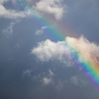 Image of a rainbow showing in a blue sky between white whisps of clouds.