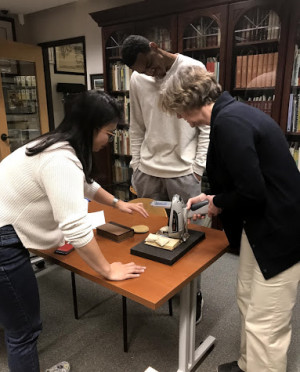 Camille Wong BA '19, Jonathan Boddie BA '18, and Valerie Walters examine a page in the book o...
